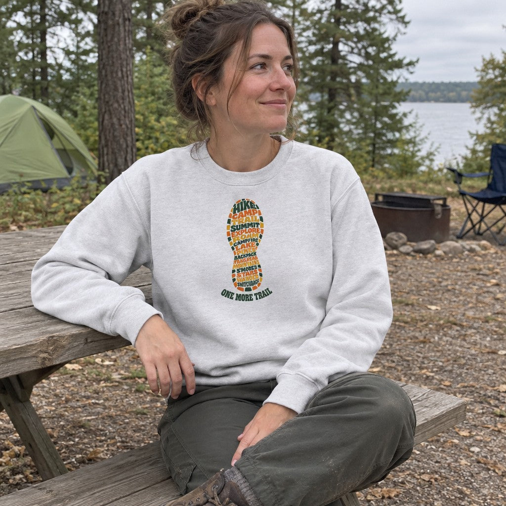 Woman wearing the One More Trail crewneck sweatshirt at a picnic table at camp
