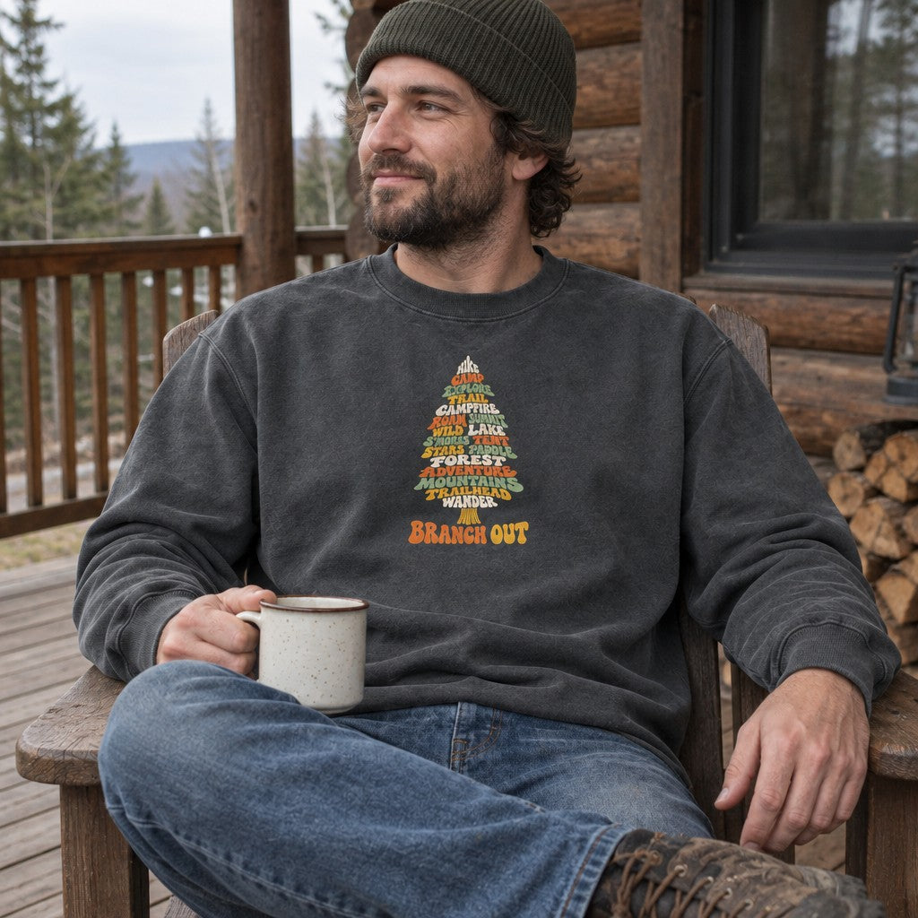 Man wearing the Branch Out crewneck sweatshirt on a cabin porch with a mug