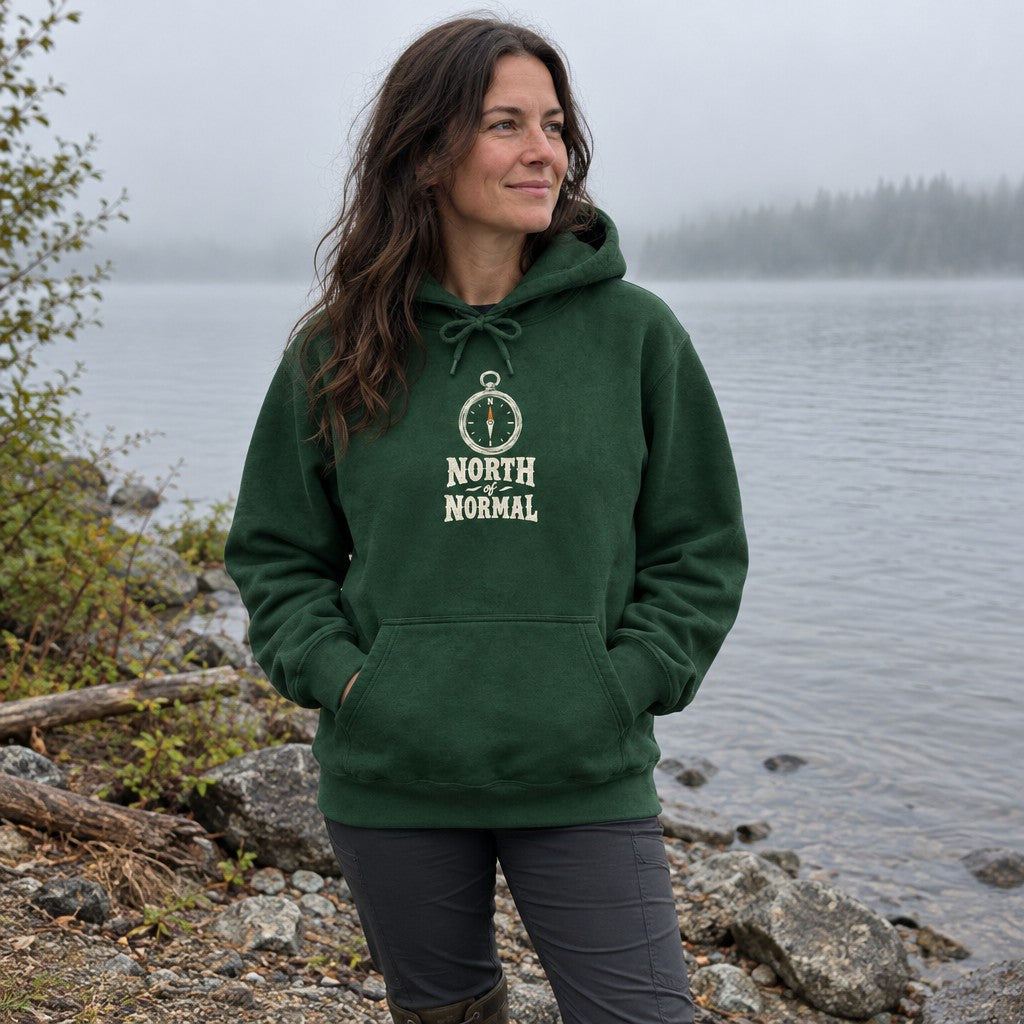 Woman wearing the North of Normal hoodie on a misty lakeshore in the morning
