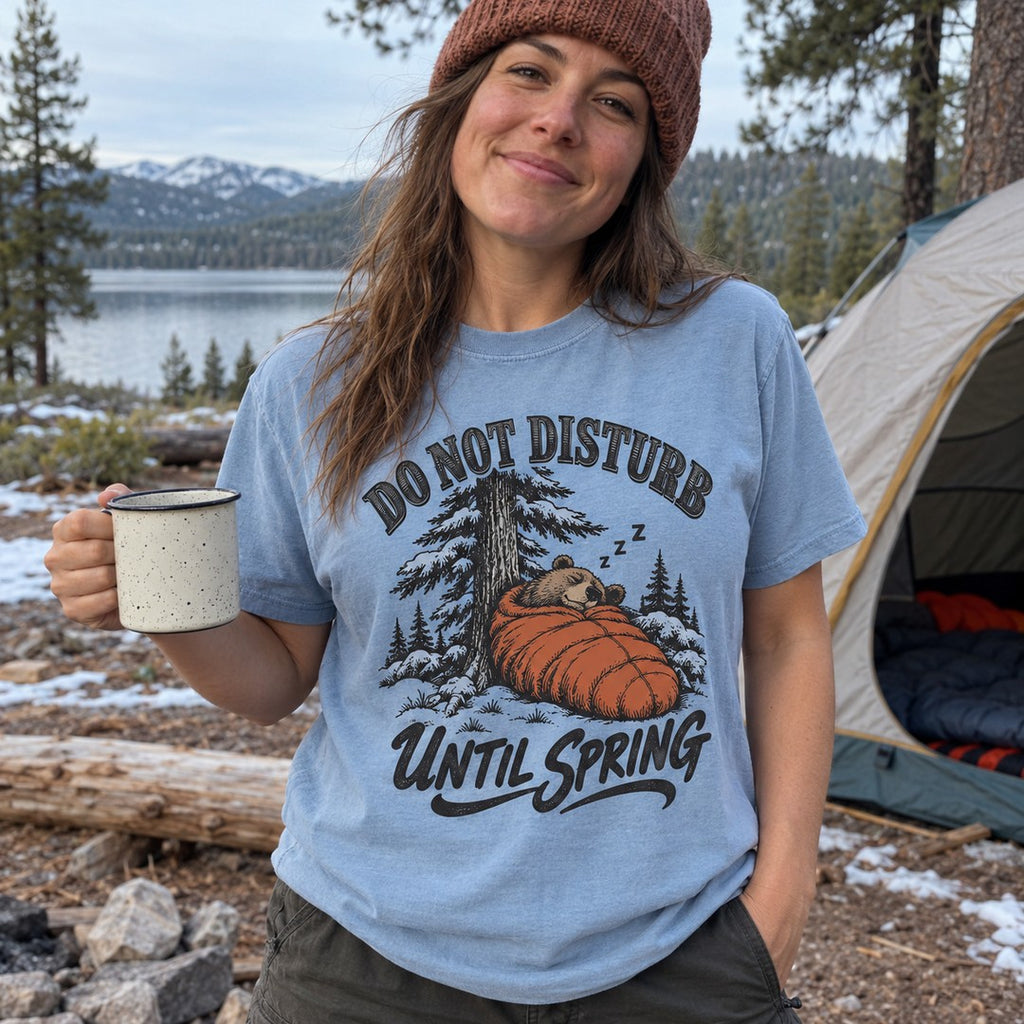 Woman wearing the Do Not Disturb Until Spring bear T-shirt at a snowy campsite