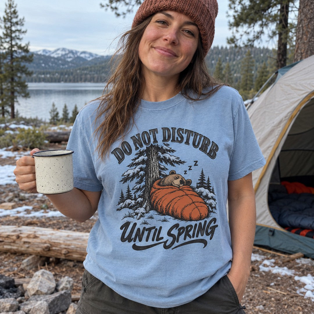 Woman wearing the Do Not Disturb Until Spring bear T-shirt at a snowy campsite
