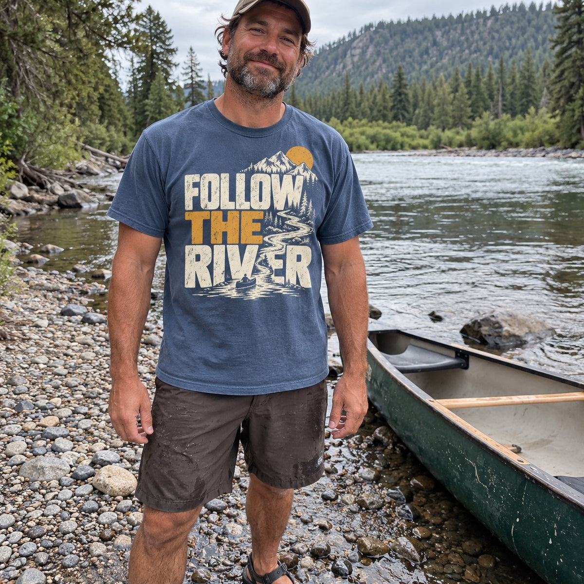 Man wearing the Follow the River T-Shirt on a riverbank next to a canoe