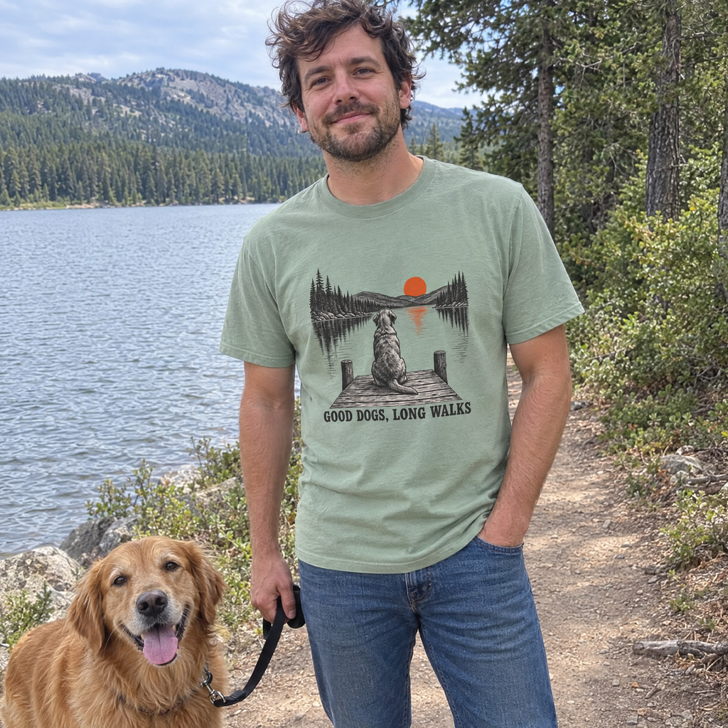 Man wearing the sage Good Dogs, Long Walks t-shirt on a lakeside trail with his golden retriever