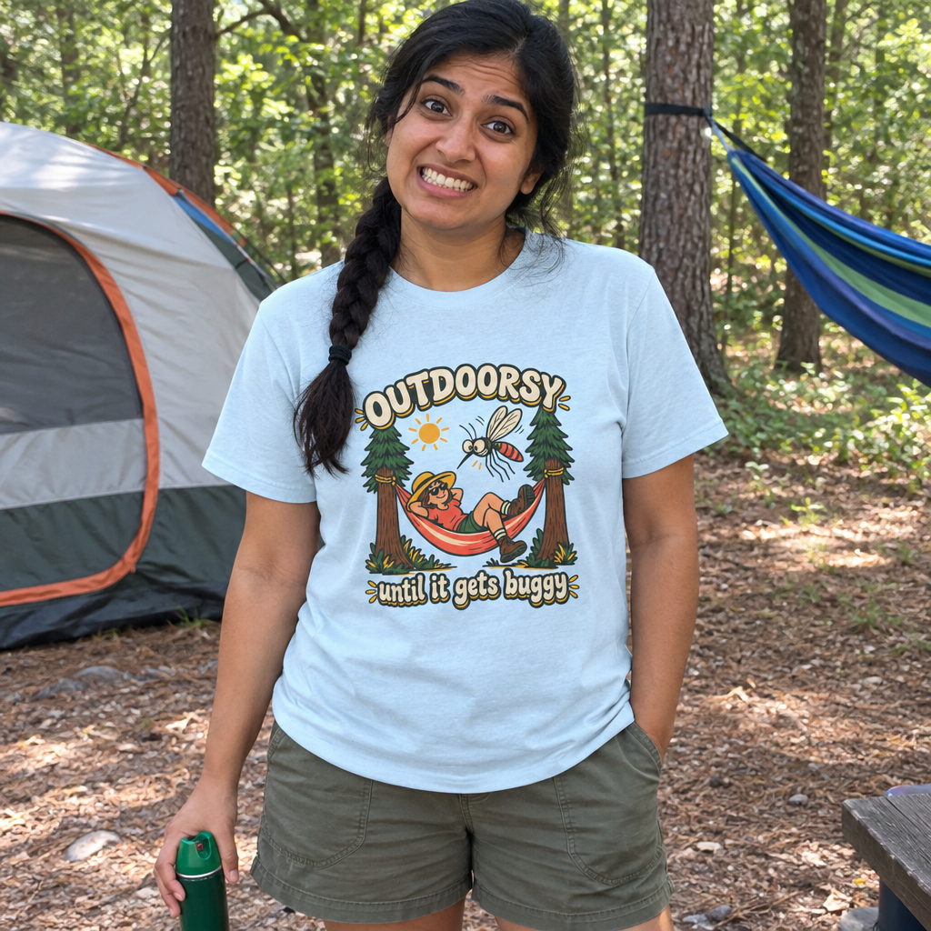 Woman wearing the light blue Outdoorsy Until It Gets Buggy t-shirt at a wooded campsite