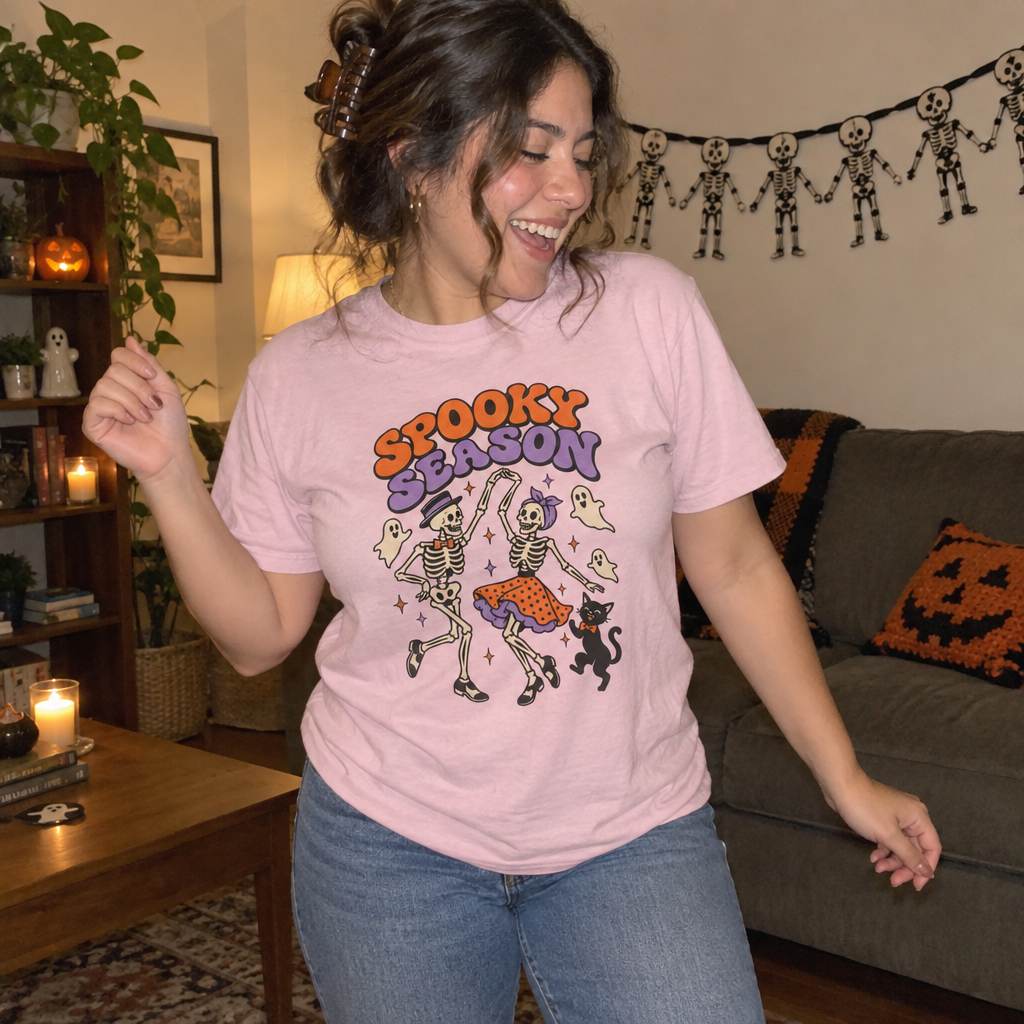 Woman wearing the pink Spooky Season Dancing Skeletons t-shirt dancing in her Halloween living room
