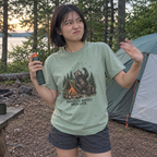 Woman wearing the sage green Mosquito Buffet. Open Late. t-shirt at a lakeside campsite