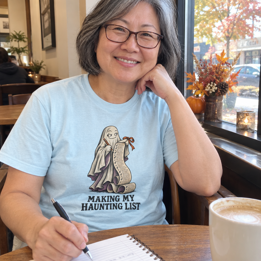 Woman wearing the light blue Making My Haunting List t-shirt at a coffee shop table