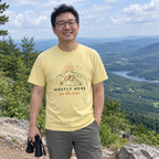 Man wearing the butter yellow Mostly Here for the View t-shirt at a mountain overlook