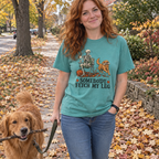 Woman wearing the seafoam Somebody Fetch My Leg t-shirt walking her golden retriever on a fall sidewalk