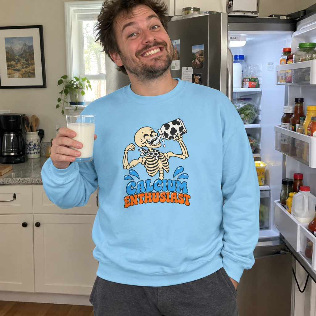 Man wearing the light blue Calcium Enthusiast sweatshirt in his kitchen with a glass of milk