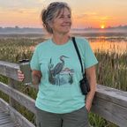 Woman wearing the mint Early Risers Welcome t-shirt on a marsh boardwalk at sunrise