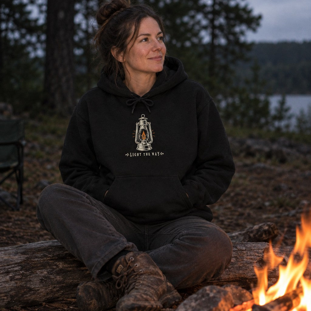 Woman wearing the Light the Way hoodie by a campfire at night