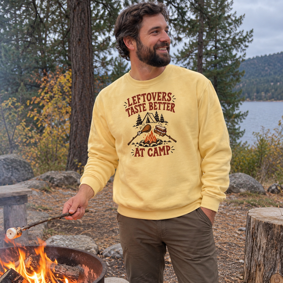Man wearing the Leftovers Taste Better at Camp Sweatshirt by a campfire with a roasting stick