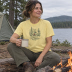 Woman wearing the Campfire & Wildflowers T-Shirt by a campfire with a mug