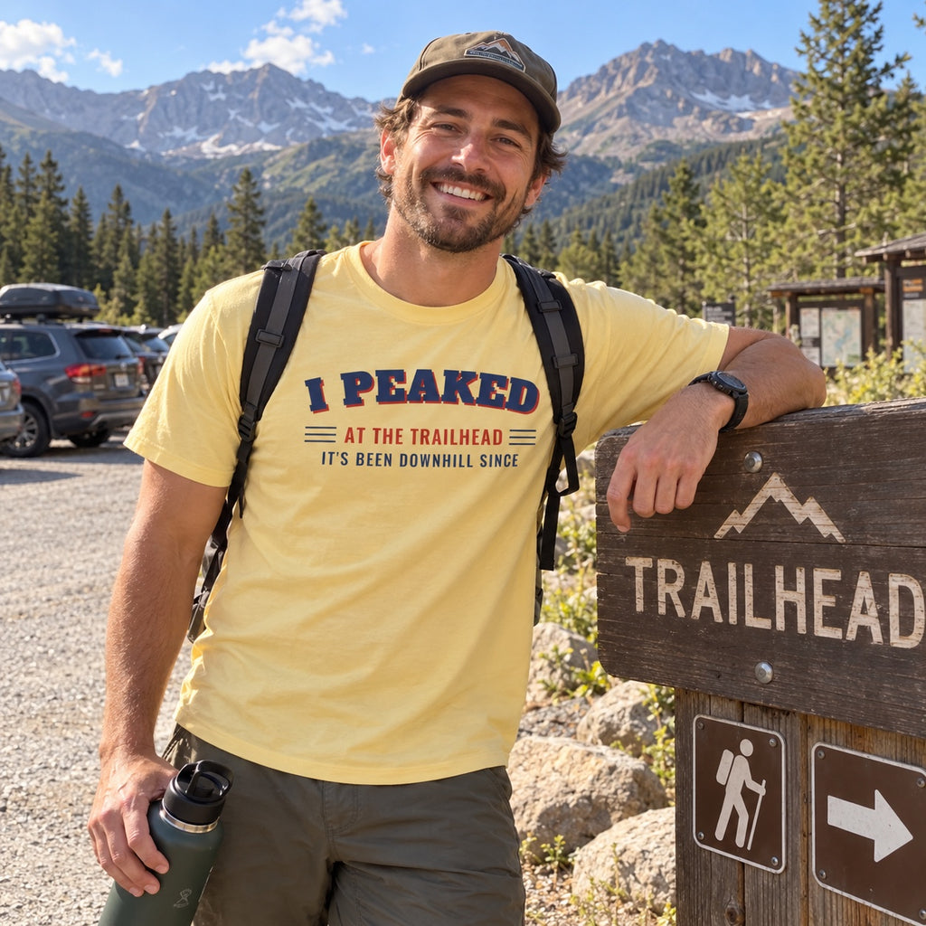 Man wearing the I Peaked at the Trailhead t-shirt next to a trailhead sign
