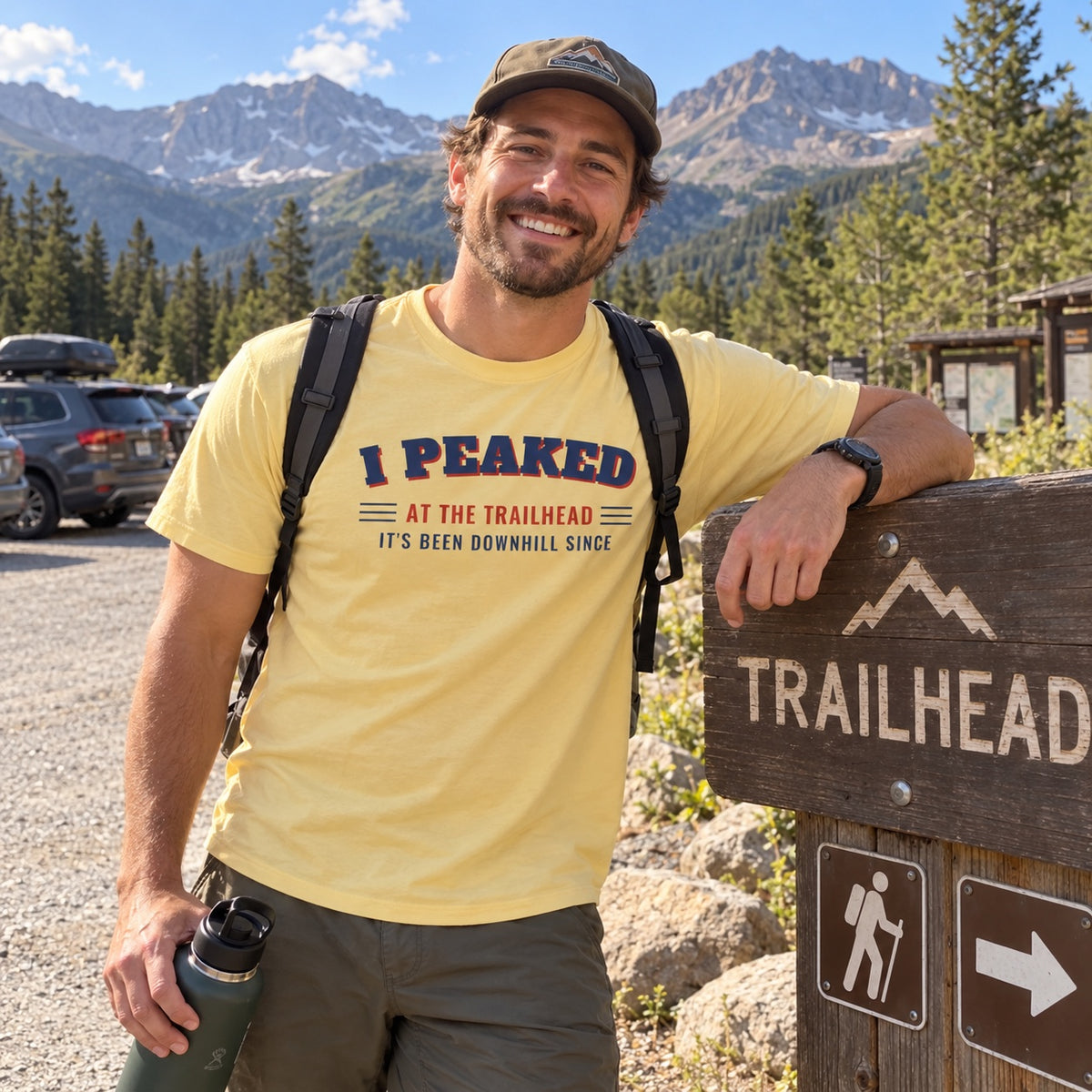 Man wearing the I Peaked at the Trailhead t-shirt next to a trailhead sign