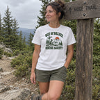 Woman wearing the Out of Breath Hiking Society Trail Sign T-Shirt resting by a wooden trail sign