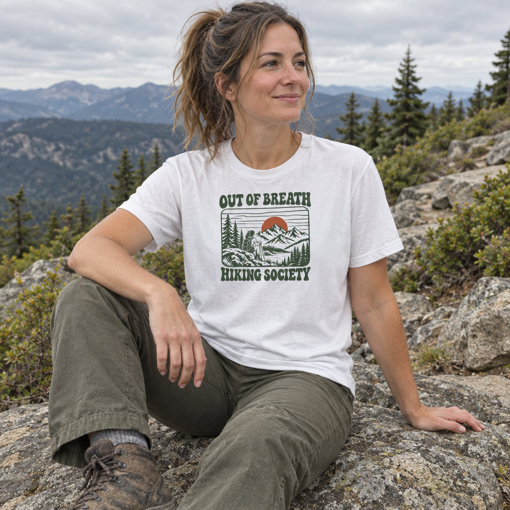 Woman wearing the Out of Breath Hiking Society Sunset T-Shirt sitting on rocks on a mountain trail