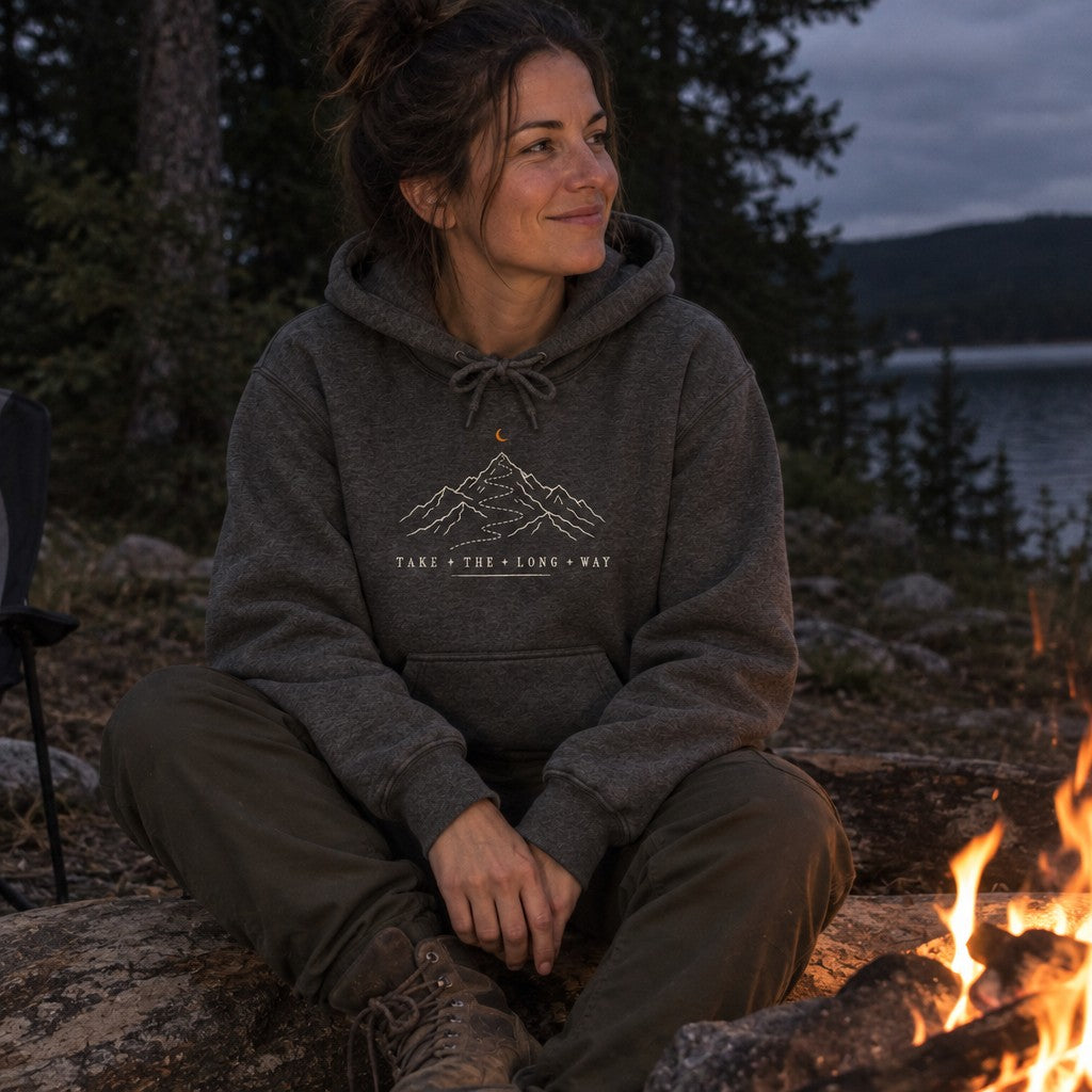 Woman wearing the Take the Long Way hoodie by a campfire at night