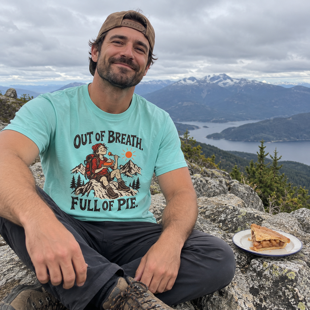 Man wearing the Out of Breath Full of Pie T-Shirt on a summit with a slice of pie