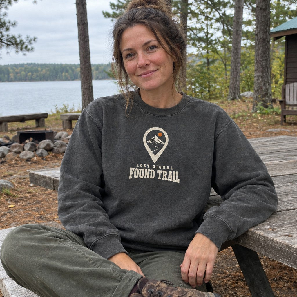Woman wearing the Lost Signal, Found Trail crewneck sweatshirt at a picnic table at camp