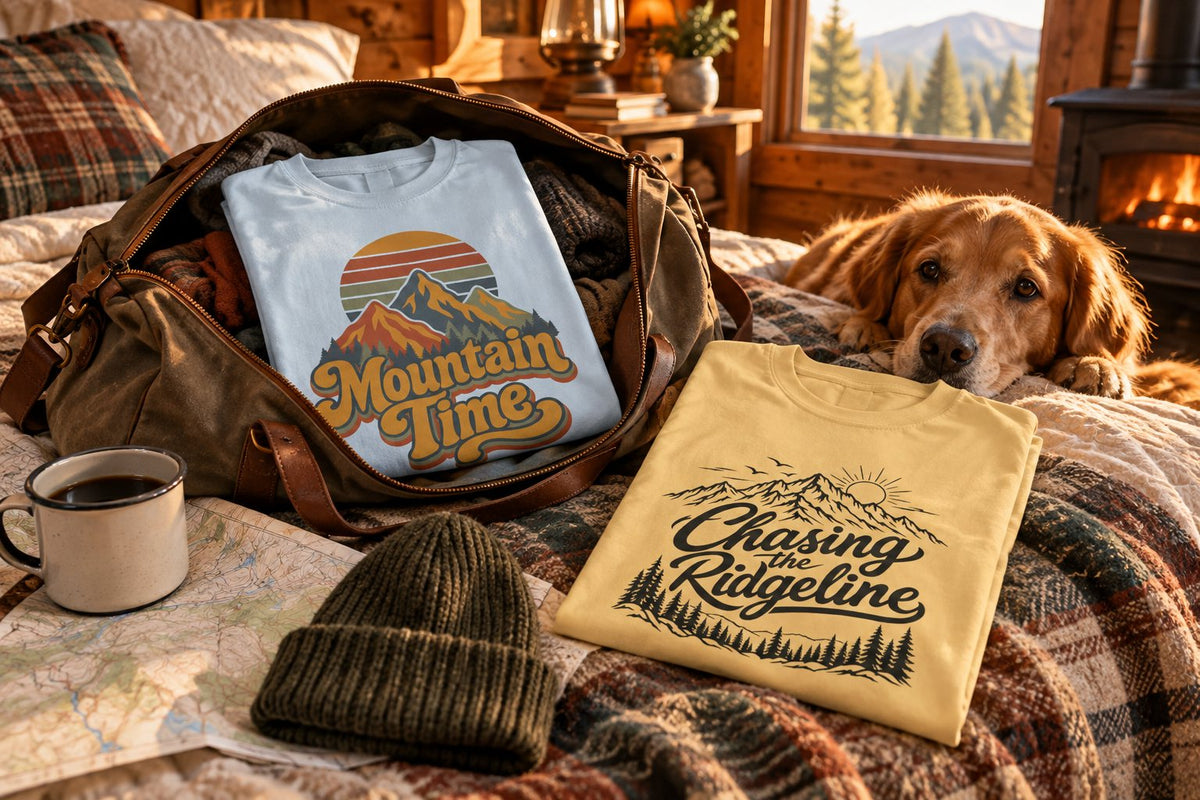 Mountain Time and Chasing the Ridgeline tees packed in a duffel on a cabin bed with a golden retriever