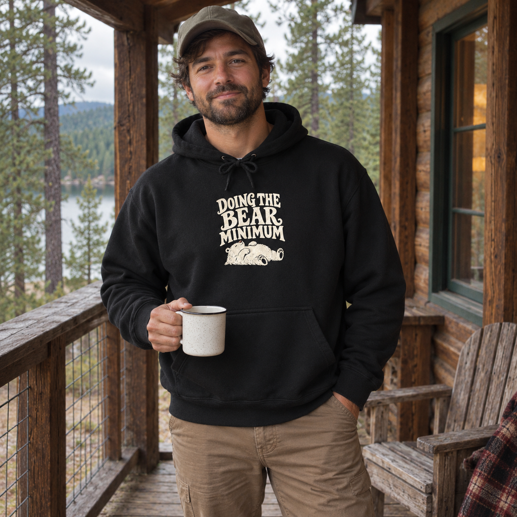 Man wearing the Doing the Bear Minimum Hoodie on a cabin porch