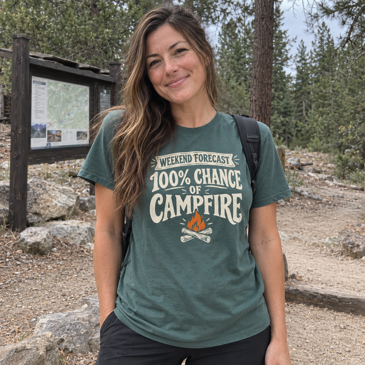 Woman wearing the Weekend Forecast: 100% Chance of Campfire T-Shirt at a lakeside campsite