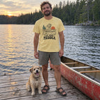 Man on a lake dock wearing the Sit. Stay. Paddle. T-Shirt with his dog