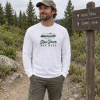 Man wearing the Slow Down Out Here long sleeve shirt at a trail sign