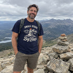 Man wearing the Small Steps, Big Views T-Shirt beside a rock cairn