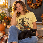 Woman on a porch with her black cat wearing the Stirring Up Trouble T-Shirt