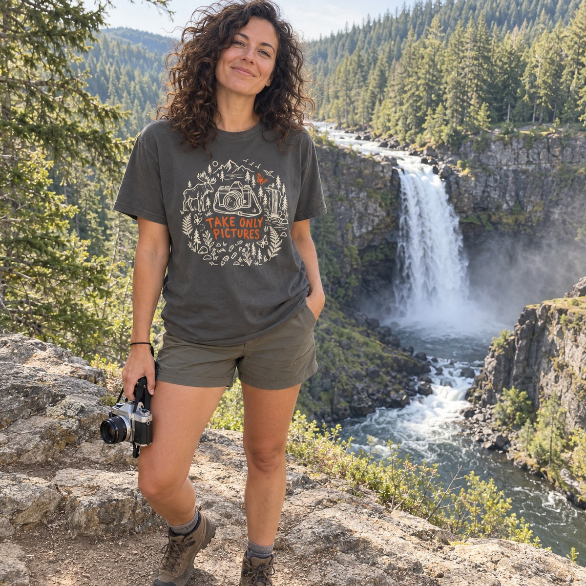 Woman wearing the Take Only Pictures T-shirt in Pepper at a waterfall