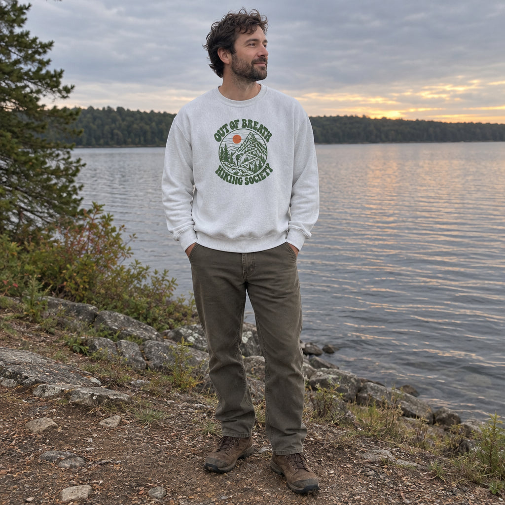 Man wearing the Out of Breath Hiking Society Switchback Sweatshirt by a lake at dusk