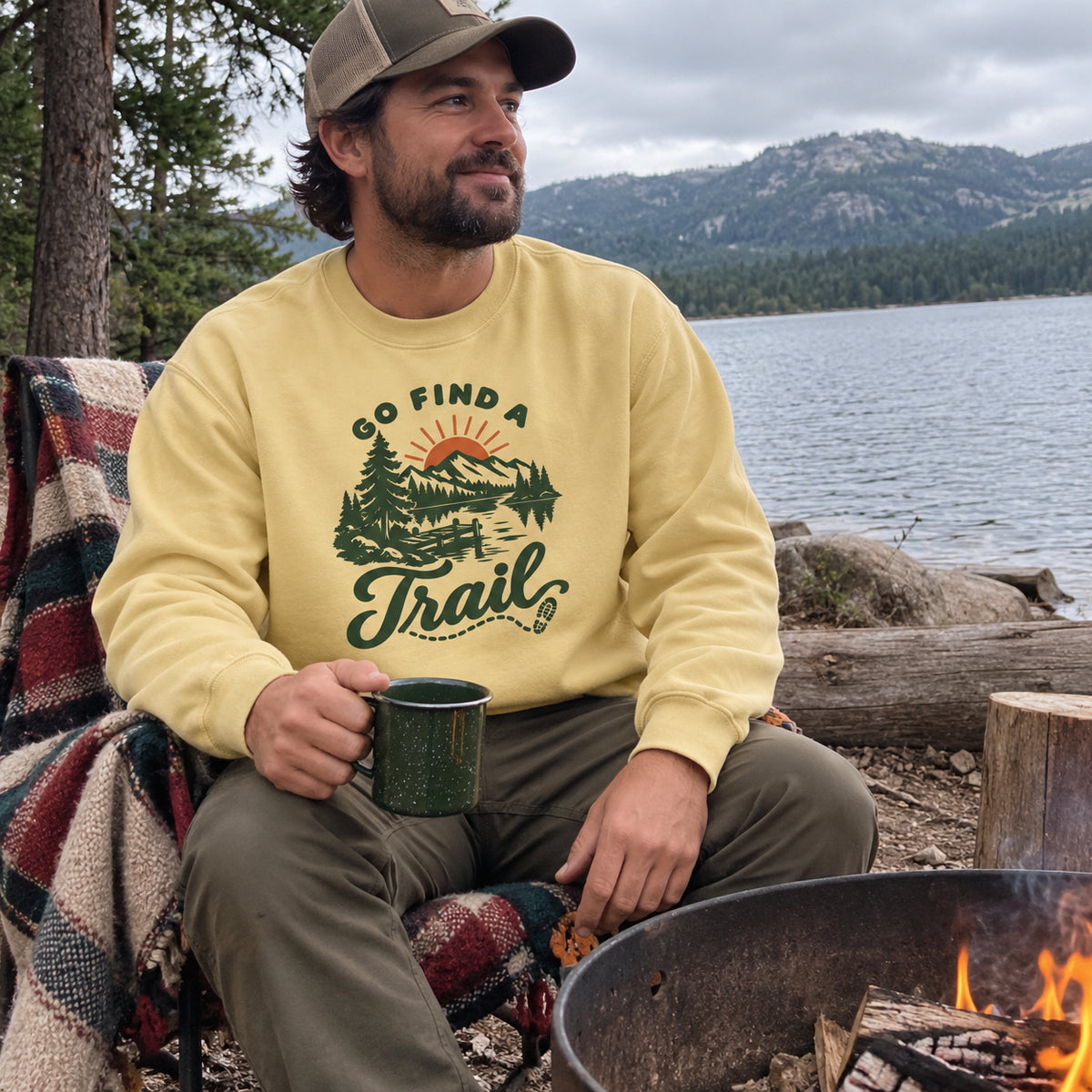 Man wearing the Go Find a Trail Sweatshirt by a lakeside fire pit with a blanket