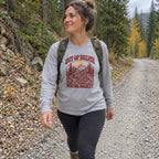 Woman wearing the Out of Breath Hiking Society Log Steps Long Sleeve Shirt walking a gravel forest road with a backpack
