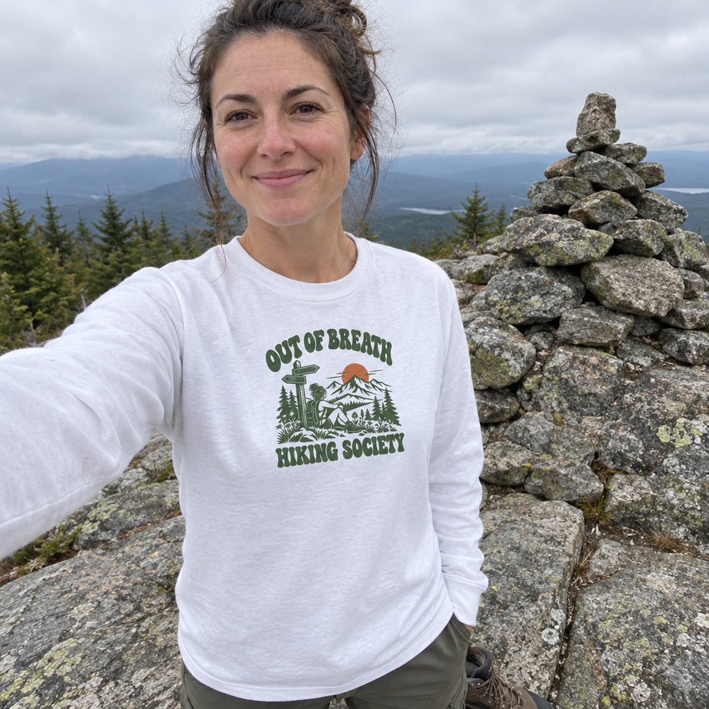 Woman wearing the Out of Breath Hiking Society Trail Sign Long Sleeve Shirt taking a selfie by a summit cairn