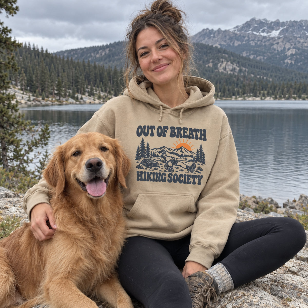 Woman wearing the Out of Breath Hiking Society Flat Out Hoodie by a lake with a golden retriever