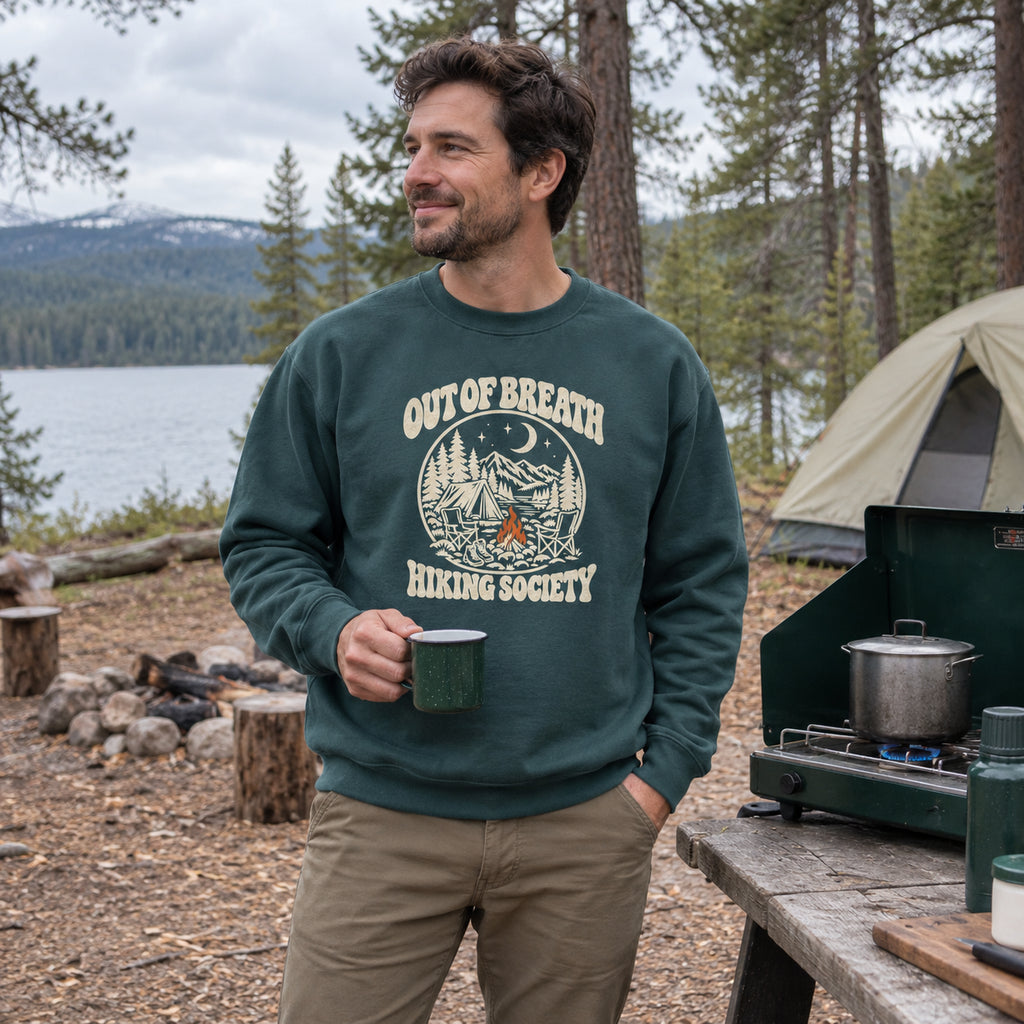 Man wearing the Out of Breath Hiking Society Campfire Night Sweatshirt standing next to a camp stove at a campsite