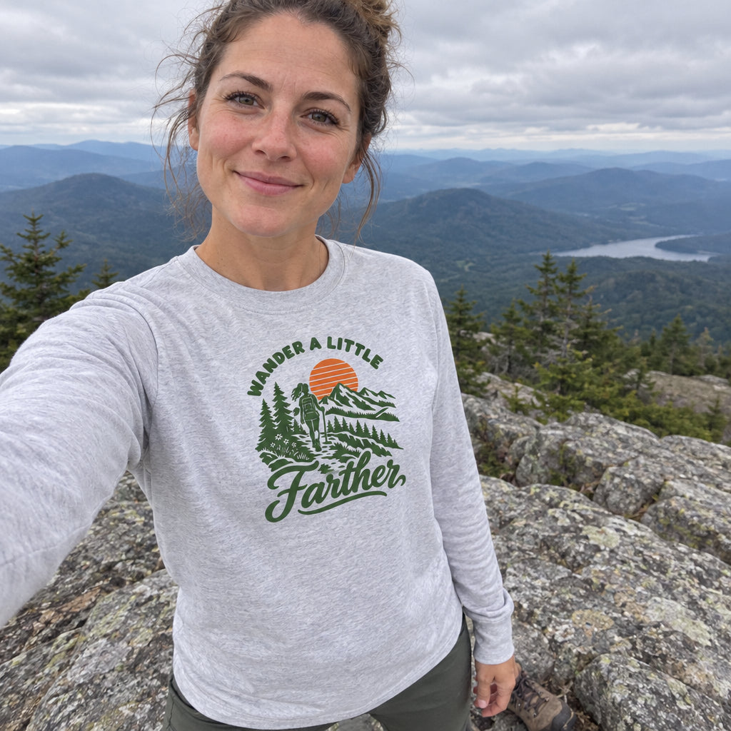 Woman wearing the Wander a Little Farther Long Sleeve Shirt taking a selfie on a mountain summit
