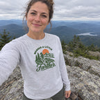 Woman wearing the Wander a Little Farther Long Sleeve Shirt taking a selfie on a mountain summit