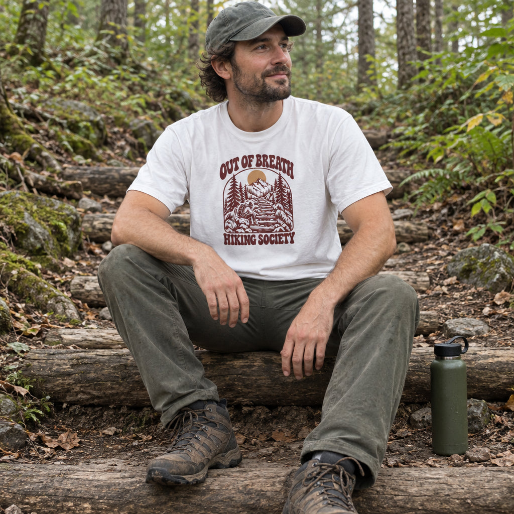 Man wearing the Out of Breath Hiking Society Log Steps T-Shirt sitting on log steps on a forest trail with a water bottle beside him