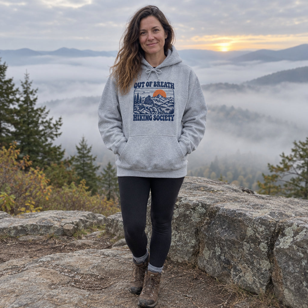 Woman wearing the Out of Breath Hiking Society Summit Rest Hoodie at a misty sunrise overlook
