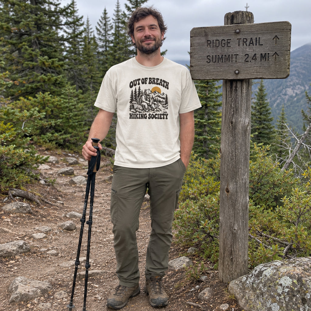 Man wearing the Out of Breath Hiking Society Bear T-Shirt by a wooden trail sign with trekking poles