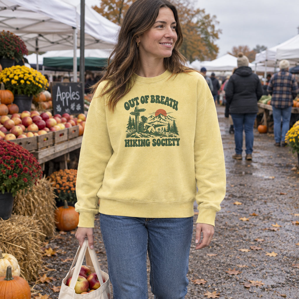 Woman wearing the Out of Breath Hiking Society Trail Sign Sweatshirt at a fall farmers market with a bag of apples