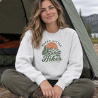 Woman wearing the Happy Little Hikes Sweatshirt sitting at a tent entrance