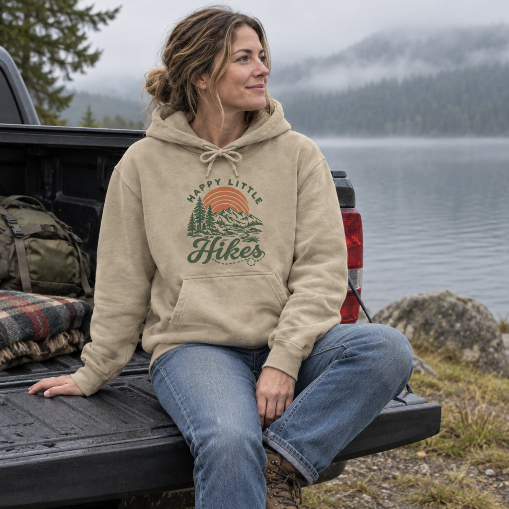 Woman wearing the Happy Little Hikes Hoodie on a truck tailgate by a misty lake