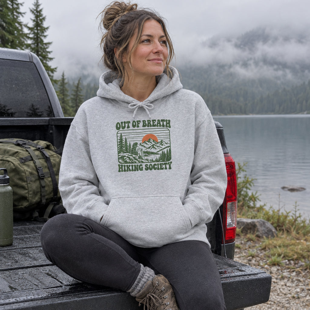 Woman wearing the Out of Breath Hiking Society Sunset Hoodie on a truck tailgate by a misty lake