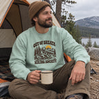 Man wearing the Out of Breath Hiking Society Bear Sweatshirt sitting at a tent entrance with a mug