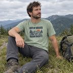 Man wearing the Out of Breath Hiking Society Flat Out T-Shirt sitting in mountain grass next to a backpack